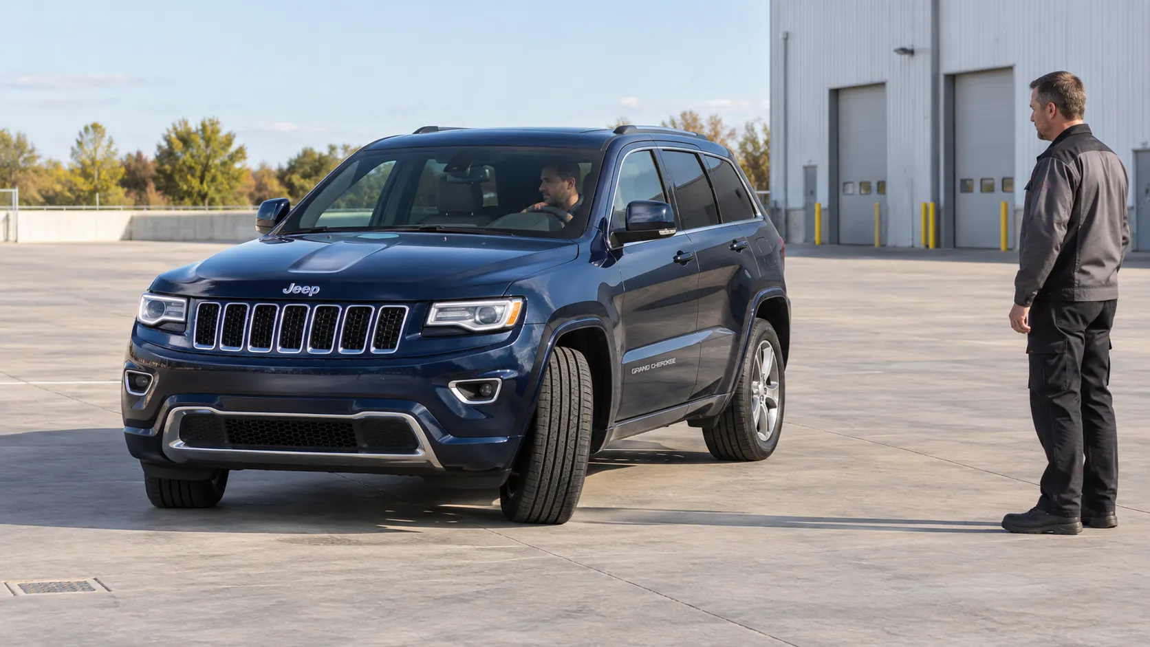 Синий Jeep Grand Cherokee WK2 с повёрнутыми колёсами на площадке сервиса под наблюдением механика